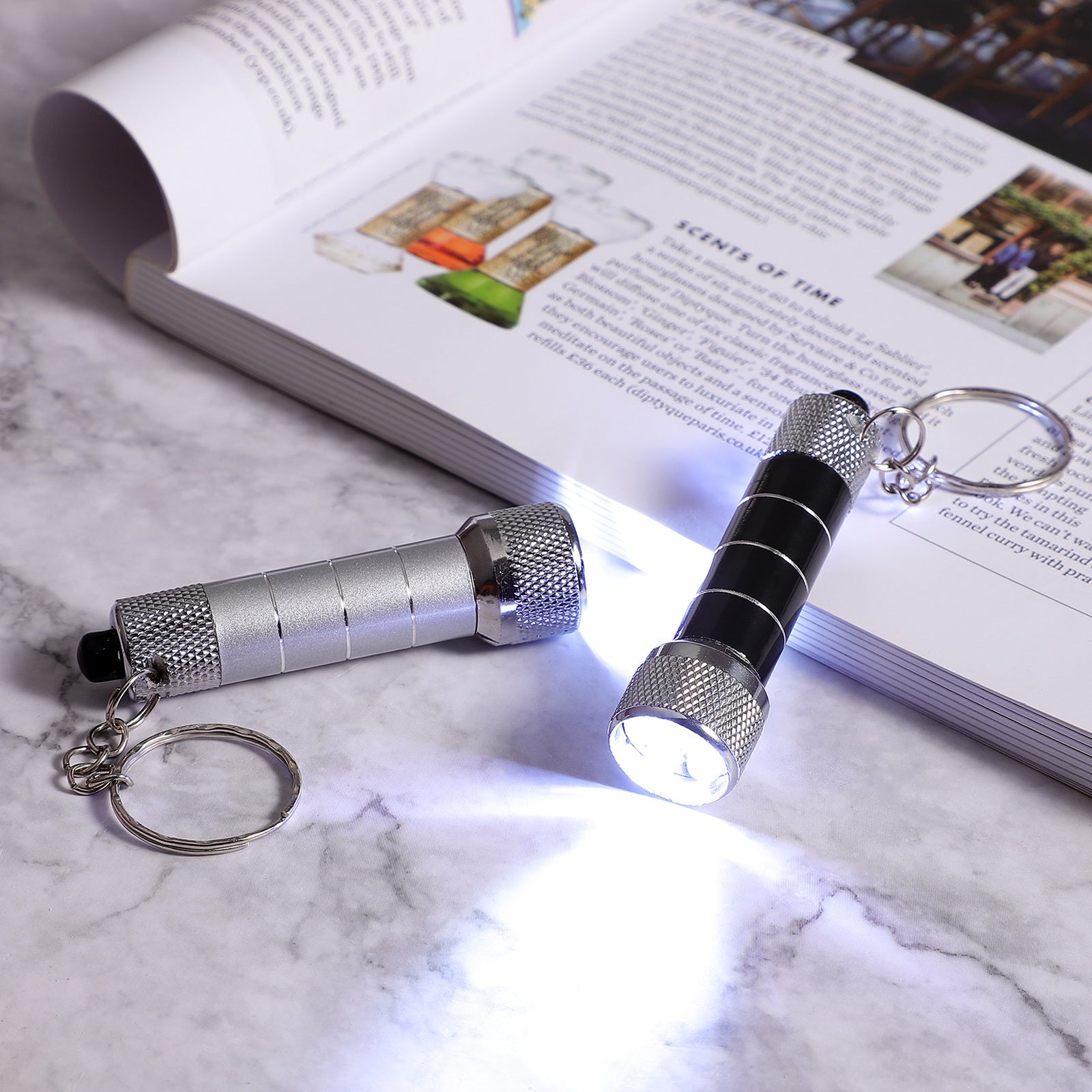 Emergency night light flashlight portable LED torch keychain on marble surface with opened book in background.