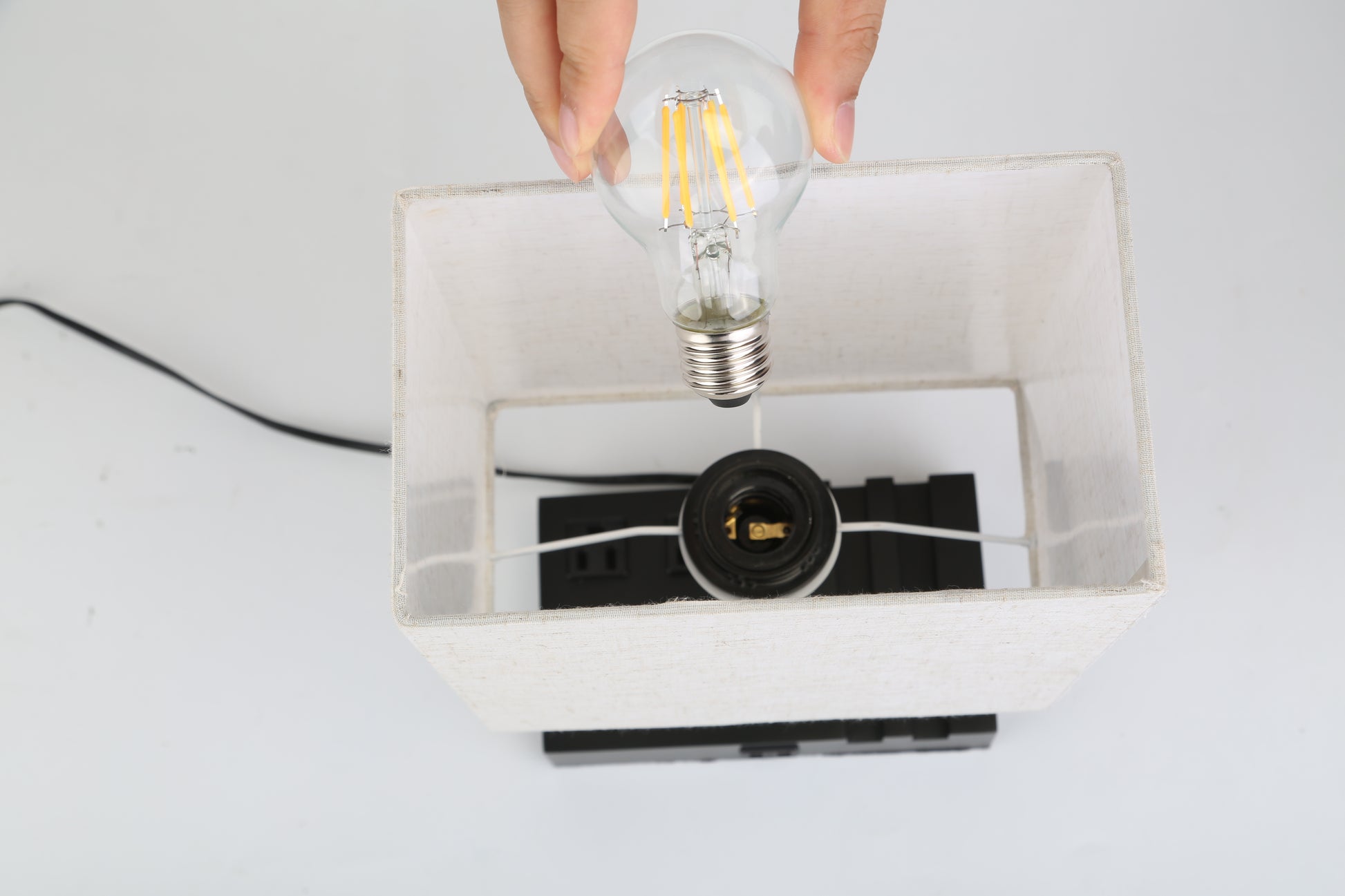 Person installing a light bulb into a fully dimmable table lamp with USB ports and power outlets.