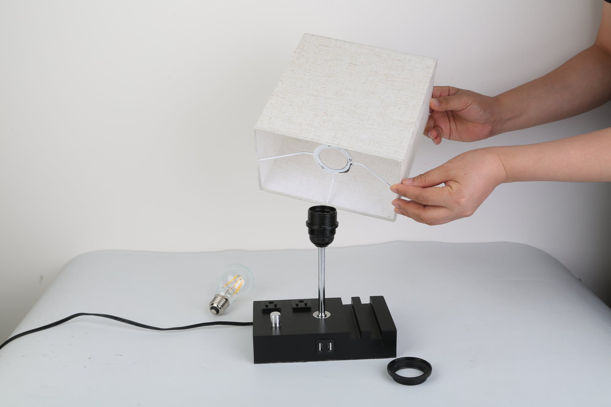 Person assembling a fully dimmable table lamp with a USB port and power outlet on a black base.